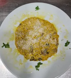 Un risotto amarillo en un plato blanco, cubierto de queso rallado y con hojas de perejil por encima.