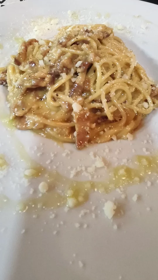 Un plato blanco grande con espaguetis en salsa cremosa, con panceta, queso rallado y pimienta, servido en la mesa.