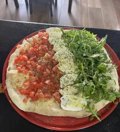 Una focaccia en un plato rojo con tomate picado, láminas de mozzarella y rúcula en tres franjas.