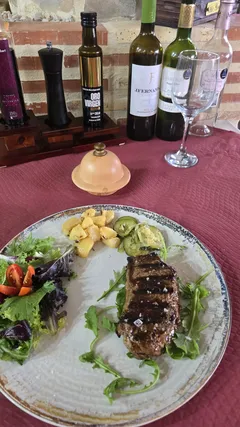 Un filete a la plancha con ensalada de brotes y dados de patata, en un plato de loza sobre mantel granate.