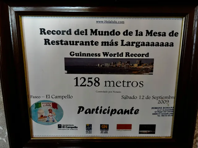 Un diploma enmarcado. Dice «Record del Mundo de la Mesa de Restaurante más Largaaaaaaa · Guinness World Record · 1258 metros · Controlado por Notario · Paseo – El Campello · Sábado 12 de Septiembre 2009» y, debajo, la palabra «Participante». Lleva el escudo del Ayuntamiento de El Campello y el óvalo del logo de Pizzería Da Marc.